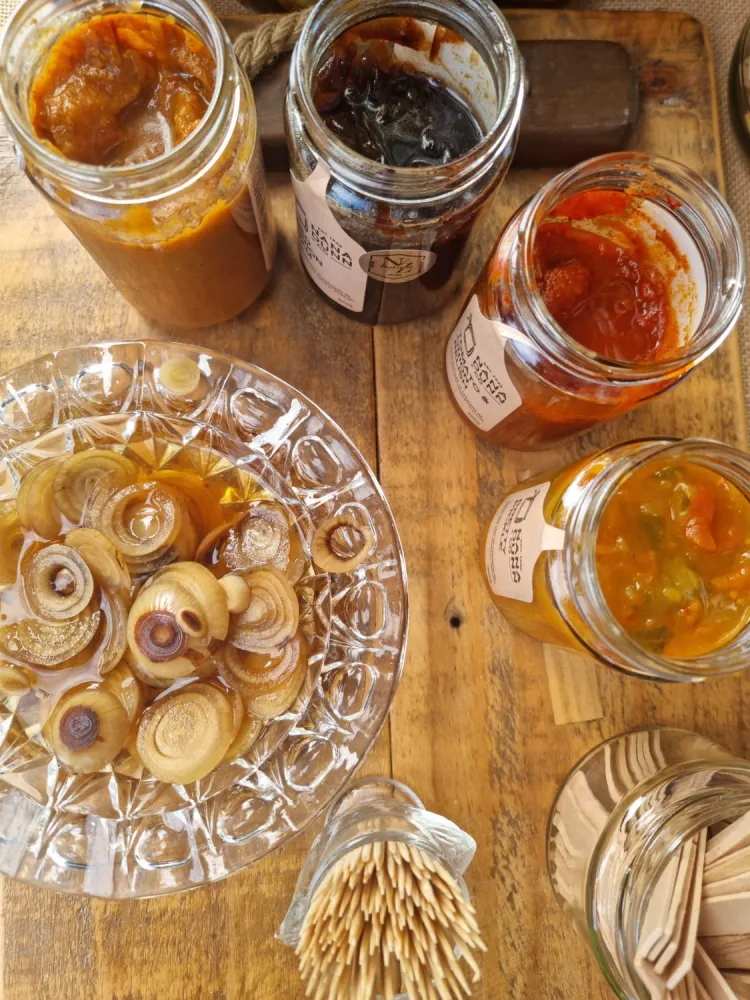 Tasting samples on a market table: pickled onions in a cut-glass bowl, open jars of chutney and relish, and toothpicks
